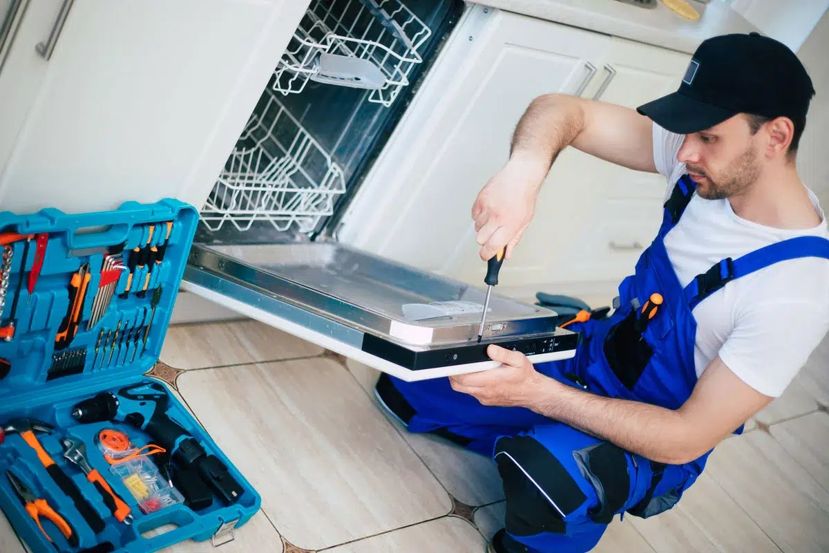 A household appliance repairman repairs a dishwasher.